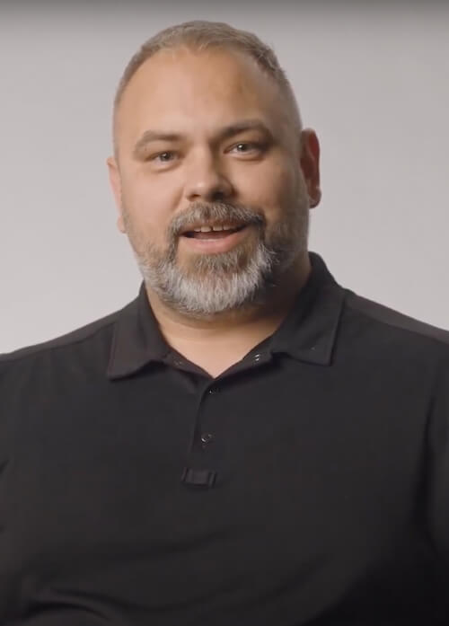 A headshot of a man in a black collared shirt